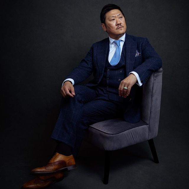 Benedict Wong posing in a suit sitting on a sofa.
